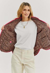 Różowa kurtka z zamkiem błyskawicznym i podszewką w panterkę, z przednimi kieszeniami i gładką zewnętrzną tkaniną, noszona na białej koszuli i jasnych spodniach.