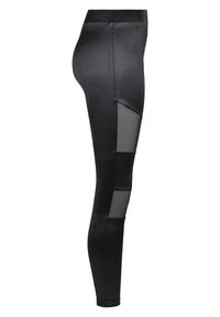 Černé legíny vyrobené z hladké tkaniny s vyřezávanými síťovinovými panely. Přiléhavý design, vysoký pas a elegantní silueta.