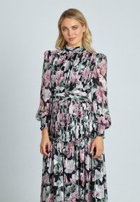 Zwarte maxi-jurk met bloemmotieven in roze en wit, lange pofmouwen, een hoge halslijn en ruches aan de onderkant.
