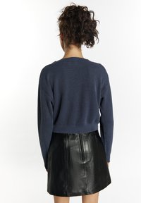 Sötétkék bordázott kötött pulóver laza szabással és cropped fazonnal, fekete bőr miniszoknyával, hátul zippes megoldással párosítva.