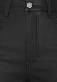 Pantalones vaqueros de mezclilla negra con una textura suave, diseño de cinco bolsillos y cierre de botón plateado en la cintura con costuras en contraste.