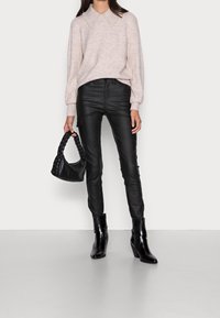 Hellrosa Pullover mit einem mit Perlen besetzten Kragen, schwarze taillierte Lederhosen und eine geflochtene schwarze Handtasche. Schwarze Stiefeletten mit Absatz.