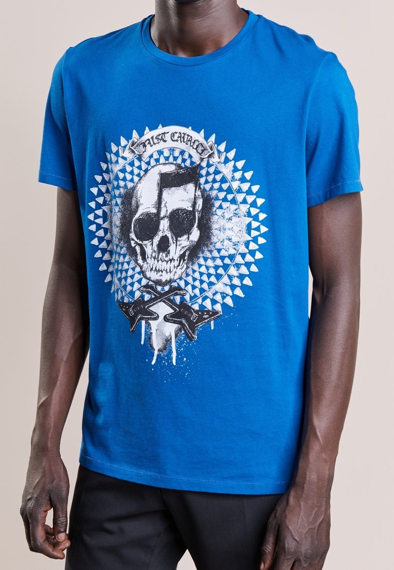 Blå bomullströja med en dödskallegrafik som har musikaliska inslag och ett cirkulärt mönster. Kortsleeves och design med rund hals.