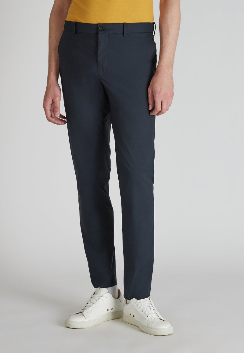 Granatowe dopasowane spodnie wykonane z lekkiego materiału, z wąskim krojem, gładkim przodem i dwoma bocznymi kieszeniami. W połączeniu z białymi sneakerami.