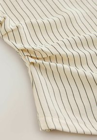 Tissu beige clair avec fines rayures verticales noires, présentant une texture douce et un design légèrement drapé avec un ourlet cousu.