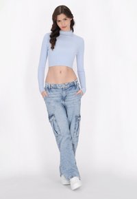 Maglia a collo alto a coste di colore azzurro chiaro, abbinata a pantaloni cargo in denim chiaro e larghi con tasche laterali. Sneakers bianche completano l'outfit.