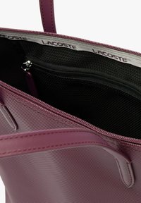 Bolso de tote texturizado en color púrpura con interior negro, bolsillo con cremallera y correas de hombro ajustables. Forrado con tela impresa con el logo.