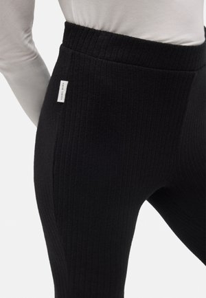 Leggings negros con canalé y cintura alta, que presentan una pequeña etiqueta de logo en el lateral. La textura es suave y elástica, proporcionando comodidad.
