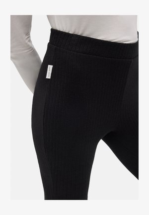Leggings negros con canalé y cintura alta, que presentan una pequeña etiqueta de logo en el lateral. La textura es suave y elástica, proporcionando comodidad.