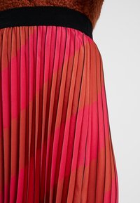 Plisovaná sukně s diagonálními červenými a oranžovými pruhy, černým pasem, spárovaná s texturovaným rustikálním topem.