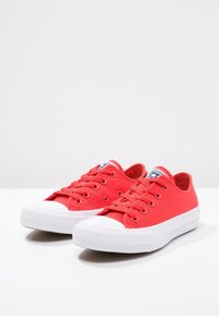 Red canvas sneakers with white rubber soles and toe caps, featuring six eyelets and laces, along with branded tongue accents.