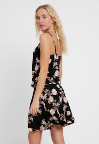 Vestido negro con estampado floral que presenta tirantes finos, un corsé ajustado y una falda acampanada con un vibrante patrón de flores en rosa y blanco.