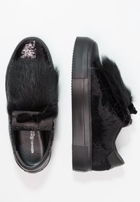 Schwarze Sneakers mit strukturiertem Obermaterial, glänzenden Pailletten und flauschigen Akzenten. Sie verfügen über eine Gummisohle und eine dekorative Schleife mit Sternenmotiven.