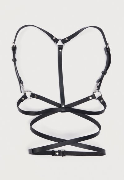 Μαύρο δερμάτινο ζυγό με λεπτές τιράντες, μεταλλικούς κρίκους και ασημί εξαρτήματα. Διαθέτει ρυθμιζόμενες πόρπες και σχεδιασμό με επικαλύψεις.