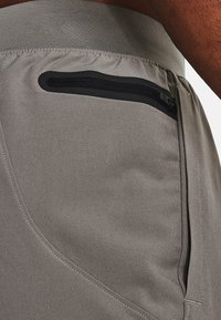 Ljust gråa träningsshorts med slim fit, elastisk midja och en dragkedjeficka med svarta dragkedjedetaljer. Slät textur.