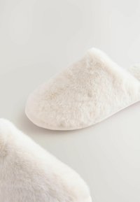 Chaussons blancs duveteux avec une texture douce et moelleuse. Forme à bout rond sans matériel ou accents visibles, avec un design sans couture.