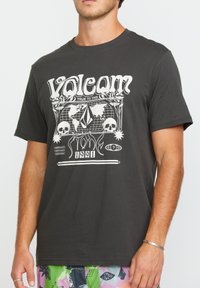 T-shirt noir à manches courtes avec un imprimé graphique blanc représentant un globe, des crânes et le texte « Volcom » et « 1991 » à l'avant. Matière en coton.