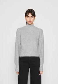 Pullover cinza em malha canelada com gola alta, mangas longas e corte cropped, combinado com calças pretas de perna larga.