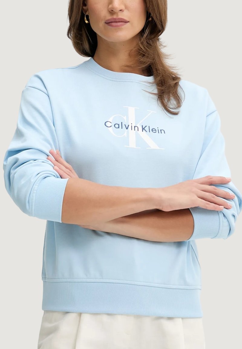 Felpa azzurro chiaro con scollo rotondo, polsini a costine e logo Calvin Klein bianco sul petto. Tessuto morbido e strutturato.