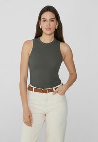Dunkelgrünes, geripptes Tanktop mit rundem Halsausschnitt, kombiniert mit hellen Hosen und einem braunen Gürtel mit metallischer Schnalle.