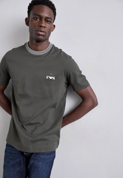 T-shirt à manches courtes vert olive avec un col rayé, ornée d'un petit logo 'EVA' brodé sur la poitrine et d'une coupe décontractée.