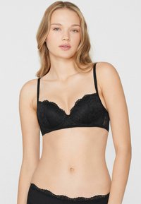 Bralette de encaje negro con escote pronunciado, bordes con ondas y tirantes ajustables. Presenta un diseño floral y soporte con aros.