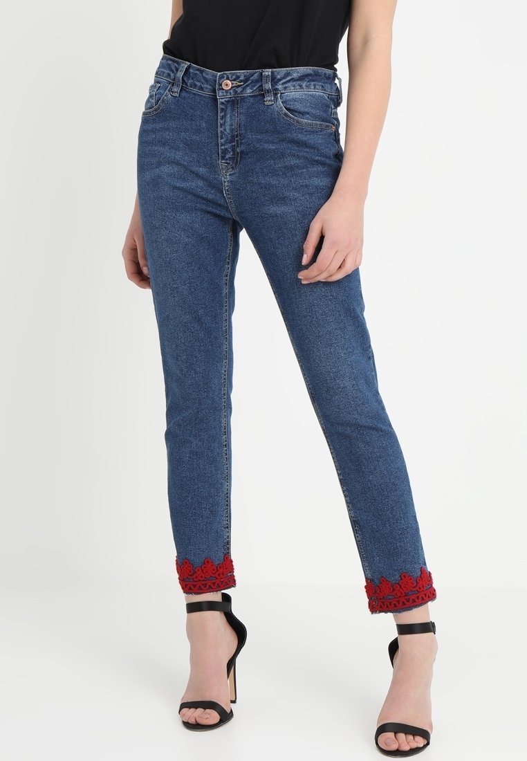 Blå denimjeans med smal passform, med röd blommig broderi vid fållarna och knappstängning. I kombination med svarta högklackade sandaler.