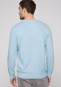 Sudadera azul claro con cuello redondo, mangas largas y puños y dobladillo de canalé. Material suave con una textura lisa. Sin patrones visibles.