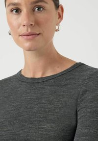 Kobieta o jasnej karnacji, nosząca srebrne kolczyki koła i ciemnoszarą koszulkę z okrągłym dekoltem, zwrócona lekko w lewo na białym tle.