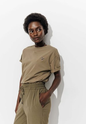 T-shirt en coton vert olive avec des manches retroussées, ornée d'une broderie en forme de cœur en imprimé léopard. Associée à un pantalon à taille élastique assorti.