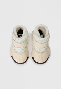Botas color crema con una parte superior suave y texturizada que presenta patrones geométricos y ondulados multicolores, suelas de goma negra y una correa de Velcro.