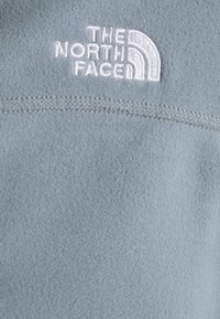 Jasnoniebieski polarowy sweter z fakturowanej powierzchni, z białym haftowanym logo "The North Face" na piersi.