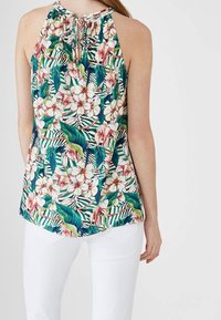 Bloemen haltertop met een levendig roze en groen patroon, voorzien van een sleutelgatdetail aan de achterkant, gecombineerd met witte broek. Gladde katoenstof.