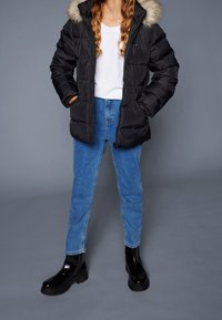 Black puffer jacket with a fur-lined hood, paired with blue jeans and shiny black ankle boots. The jacket features side pockets and a zip closure.
