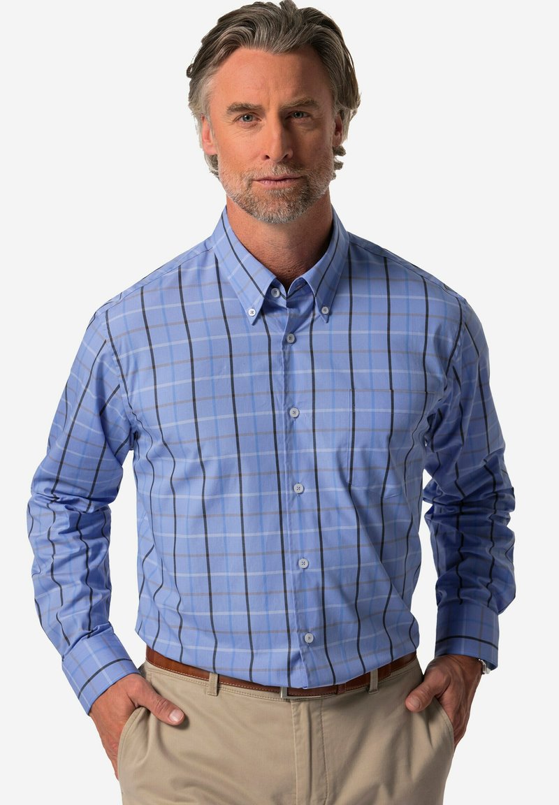 Camicia button-down a quadri blu chiaro con righe blu scuro e bianche, maniche lunghe e una tasca sul petto. Indossata con pantaloni beige.