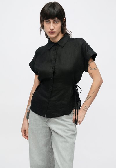 Μαύρο πουκάμισο από λινό με κοντά μανίκια, γιακά, κουμπιά στο μπροστινό μέρος και δεσίματα στο πλάι. Το ελαφρώς υφασμένο ύφασμα προσθέτει οπτικό ενδιαφέρον.