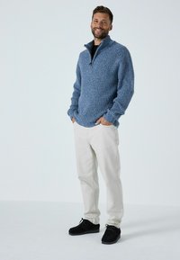 Gaiši zils, ribots adījums ar ceturtdaļas rāvējslēdzēja apkakli, apvienots ar gaiši bežām biksēm un melnām kurpēm. Vienkārša, ikdienišķa apģērba izvēle.