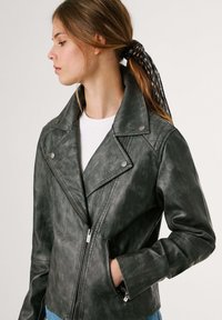 Mustast nahast mootorrattajakist, millel on terav krae, diagonaalne lukku ja küljetaskud; omaduseks on veidi kulunud tekstuur.