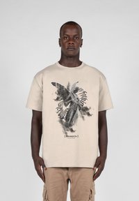 Beige bomulds t-shirt med en sort-hvid engel grafik og teksten "[Вечность]" nedenfor, korte ærmer og en afslappet pasform.