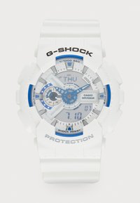 Montre G-SHOCK blanche avec des accents bleus. Affichages numériques et analogiques, bracelet texturé, étanche jusqu'à 20 bars, boutons étiquetés et cadran clair.