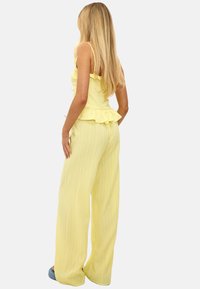 Conjunto de dos piezas amarillo que presenta una blusa con volantes y pantalones de pierna ancha. La tela tiene un acabado texturizado, mostrando un diseño ligero y fresco.