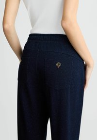Pantalon bleu marine à taille élastique avec deux poches arrière, doté de garnitures en or et d'une texture subtile, créant une apparence mouchetée.
