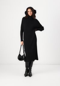 Long black ribbed knit dress with a high neck and long sleeves, paired with black faux fur earmuffs and a small black handbag.