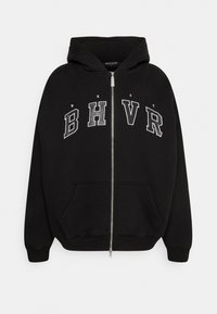 Felpa nera con zip realizzata in tessuto morbido, dotata di cappuccio, tasche frontali e lettere 'WRST BHVR' ricamate in grigio sul petto.