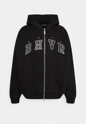 Sudadera negra con cremallera hecha de tela suave, con capucha, bolsillos frontales y letras bordadas 'WRST BHVR' en gris en el pecho.