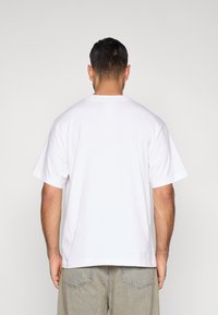 T-shirt branca de algodão com decote redondo e mangas curtas, apresentando um ajuste descontraído. Sem logotipos ou padrões visíveis. Usada com calções de ganga cinzentos.