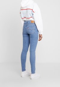 Jeans ajustados azules de mezclilla, con un clásico diseño de cinco bolsillos, parche de cuero en la parte trasera y un ligero desgaste en los muslos.