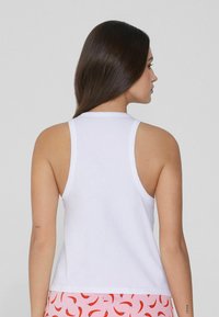 Camiseta sin mangas de algodón blanca con escote redondo y tirantes anchos. Textura suave, diseño ajustado, la vista trasera muestra las sisas y una ligera curva en el dobladillo.