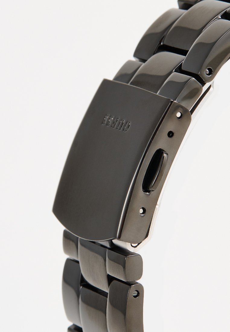 Reloj de metal negro con diseño de pulsera de eslabones. Presenta un acabado mate, cierre oculto y una caja rectangular suave con bordes elevados.