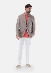Hellgrauer karierter Blazer über einem korallenfarbenen Poloshirt, kombiniert mit weißen Hosen und beigen Schuhen. Glatter Stoff mit strukturiertem Schnitt und Taschen.